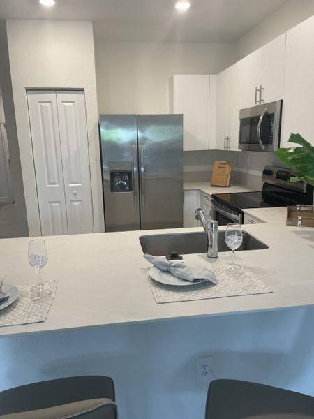 A modern kitchen with sleek stainless steel appliances, white cabinetry, and a breakfast bar setup for dining.