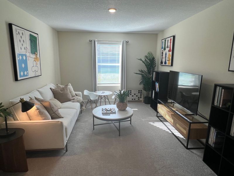 A cozy living room with a white sofa, modern art, and a sleek media setup. Bright and inviting with natural light.