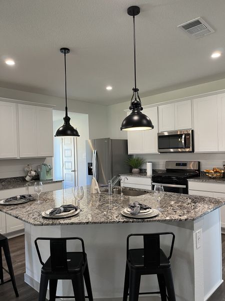 Modern kitchen with granite island, stainless appliances, white cabinets, and black pendant lights.