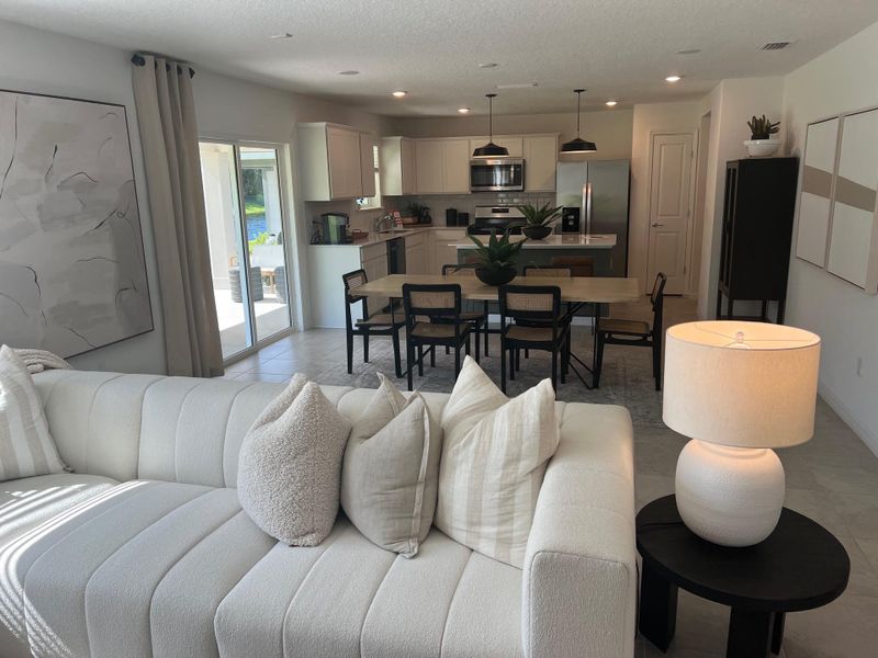 A modern living space with a cozy white sofa, stylish dining area, and sleek kitchen featuring pendant lighting and minimalist decor.