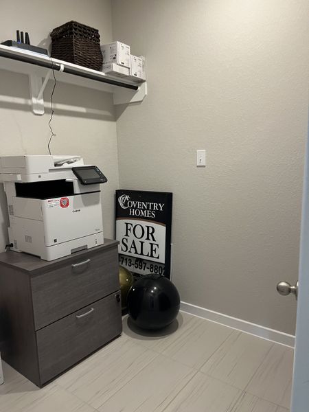 A compact office nook featuring a printer, storage cabinet, and wall shelving for organized functionality.