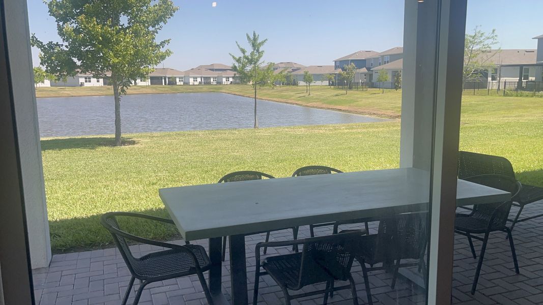 A serene patio with a large table overlooks a tranquil pond and manicured lawn, offering a perfect relaxation spot.