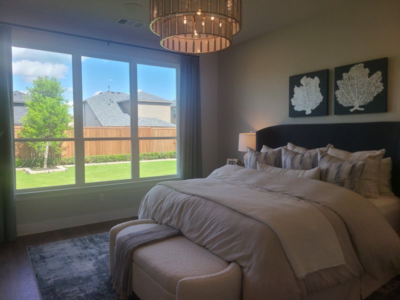 A cozy bedroom featuring a plush bed, large window with garden view, elegant chandelier, and modern art decor.