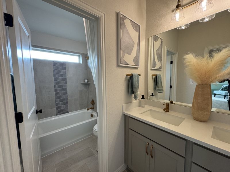 A modern bathroom with a sleek vanity, gold fixtures, abstract art, and a stylish bathtub with decorative tile accents. A modern bathroom with a sleek vanity, gold fixtures, abstract art, and a stylish bathtub with decorative tile accents.