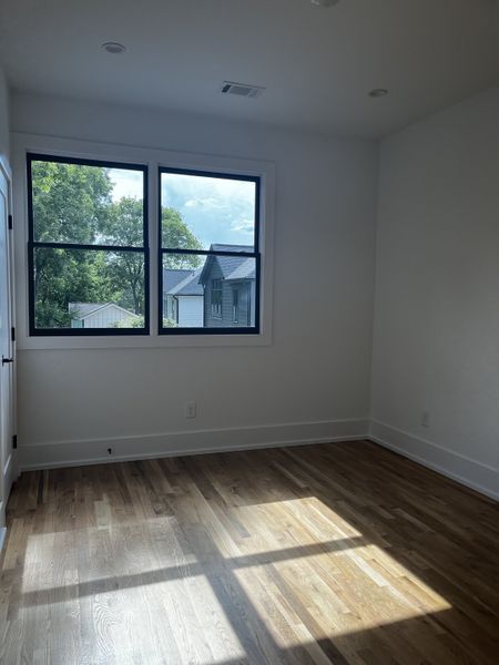 A bright room with hardwood floors, white walls, and large windows offering serene views of the surrounding greenery.