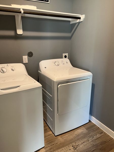 A modern laundry room with sleek appliances and a wooden floor, featuring practical shelving and soothing gray walls.