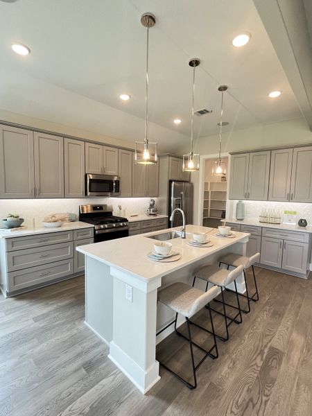 A modern kitchen with sleek gray cabinetry, a spacious island, stylish pendant lighting, and stainless steel appliances.