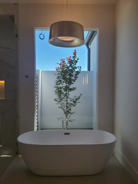 A modern bathroom showcasing a sleek free-standing bathtub, large window, and elegant pendant lighting.
