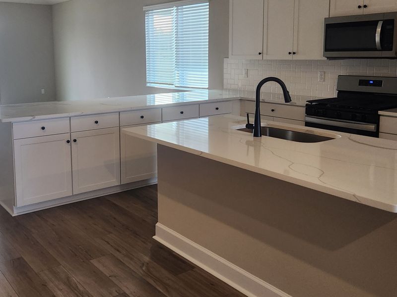 Modern kitchen featuring sleek white cabinetry, stone counters, stainless appliances, and elegant flooring.