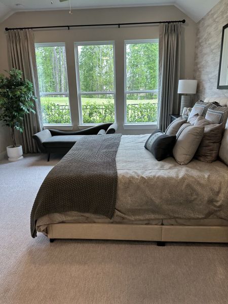 A serene bedroom with large windows, cozy bedding, and elegant decor overlooking a lush green view.