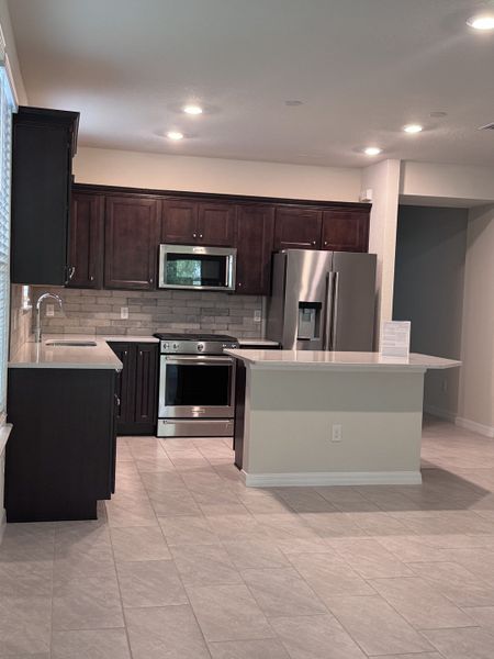 A modern kitchen with dark cabinetry, stainless steel appliances, sleek countertops, and ample natural light.