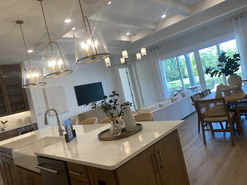 A bright open-concept living area with elegant pendant lights, cozy seating, and expansive window views of lush greenery.