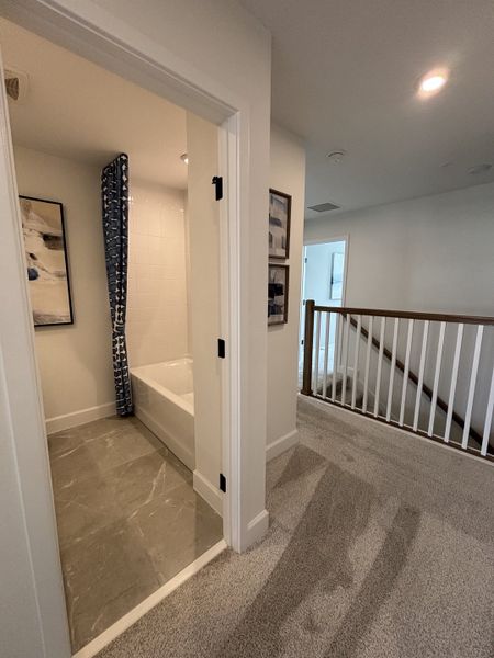 A cozy hallway with plush carpeting, a sleek bathroom with gray tiles, modern fixtures, and artful accents.