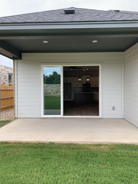 A modern backyard patio with sliding glass doors leading to the interior, displaying lush grass and a sleek overhang.