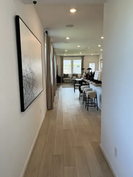 A sleek hallway featuring light wood flooring, large art piece, and modern seating leading to a cozy living area. A sleek hallway featuring light wood flooring, large art piece, and modern seating leading to a cozy living area.