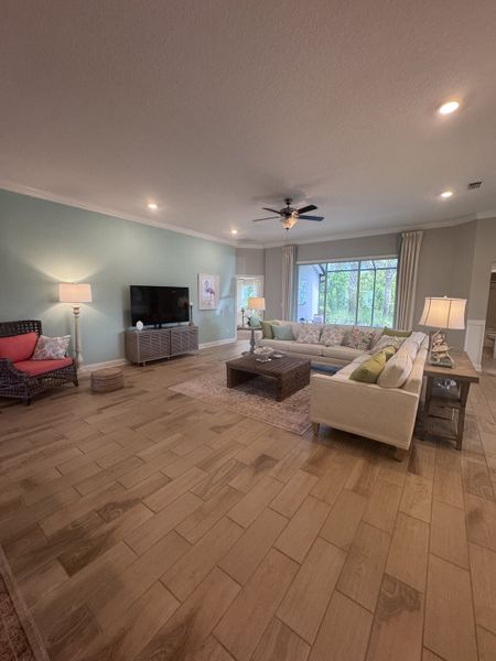 A spacious living room with wood flooring, cozy sectional sofa, and large windows offering natural light.