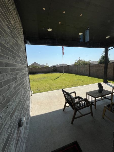 A cozy patio with seating overlooks a neatly fenced yard, perfect for relaxation and outdoor enjoyment.