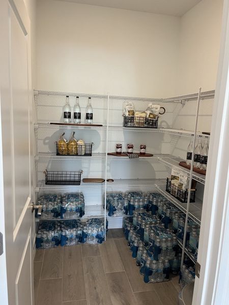 A spacious pantry with organized shelves, neatly stocked with bottled water and various dry goods, featuring sleek tile flooring.