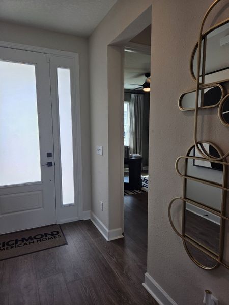 A modern entryway with sleek flooring, decorative mirror, and inviting natural light. Richmond American Homes mat by the door.