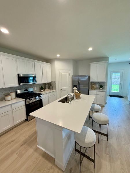 A modern kitchen boasts white cabinetry, sleek countertops, and a central island with barstools, creating a bright, inviting space.