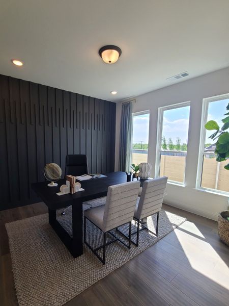 A contemporary office with a sleek black feature wall, large windows, and modern furnishings on a textured rug.