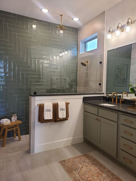 A stylish bathroom with green herringbone tiles, a sleek black countertop, and elegant gold fixtures. A stylish bathroom with green herringbone tiles, a sleek black countertop, and elegant gold fixtures.