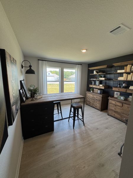 A cozy home office with a rustic wood desk, open shelving, and natural light through large windows.