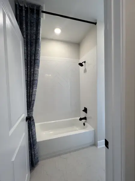 A modern bathroom featuring a herringbone-tiled bathtub, black fixtures, and a patterned curtain.