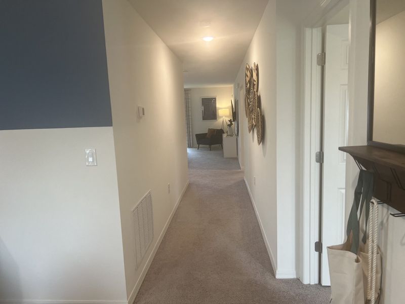 A bright hallway with soft carpet, modern decor, and a view into a cozy, warmly lit seating area.