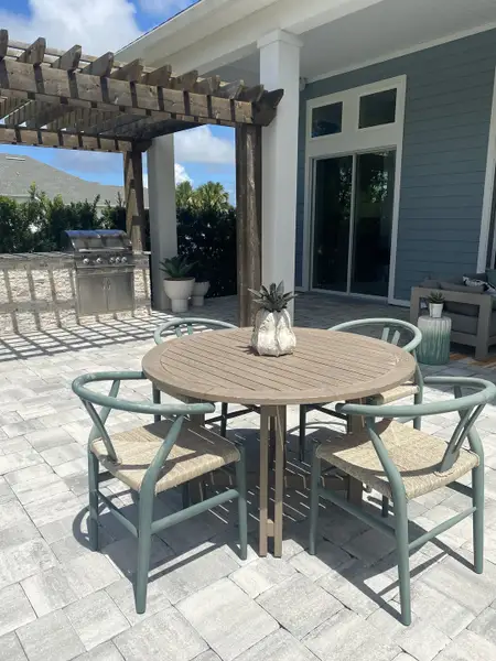 A chic patio with a round wooden table, modern chairs, a pergola, and a built-in grill, perfect for outdoor gatherings.