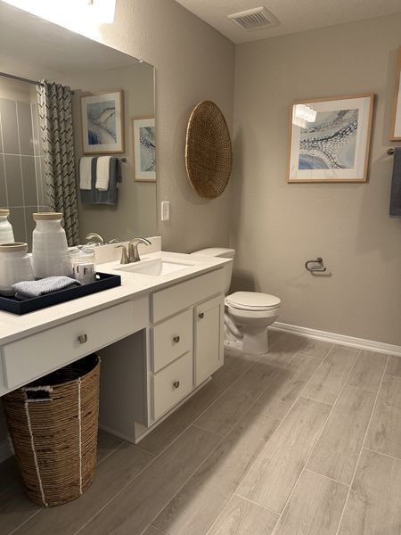 A modern bathroom with a sleek vanity, woven wall decor, and chic artwork, creating a serene and stylish atmosphere.