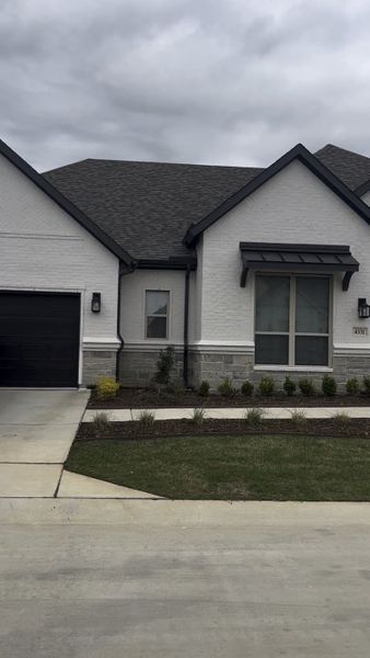 A modern white brick home with dark accents and a manicured lawn in Ladera Prosper by Ladera Texas (Prosper, TX). A modern white brick home with dark accents and a manicured lawn in Ladera Prosper by Ladera Texas (Prosper, TX).