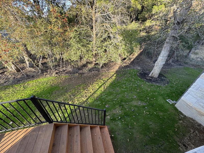 A tranquil backyard with a view of lush trees and a well-maintained lawn seen from a wooden deck staircase.
