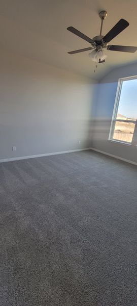 A spacious bedroom with plush carpeting, neutral walls, and a ceiling fan, featuring a large window for ample natural light.