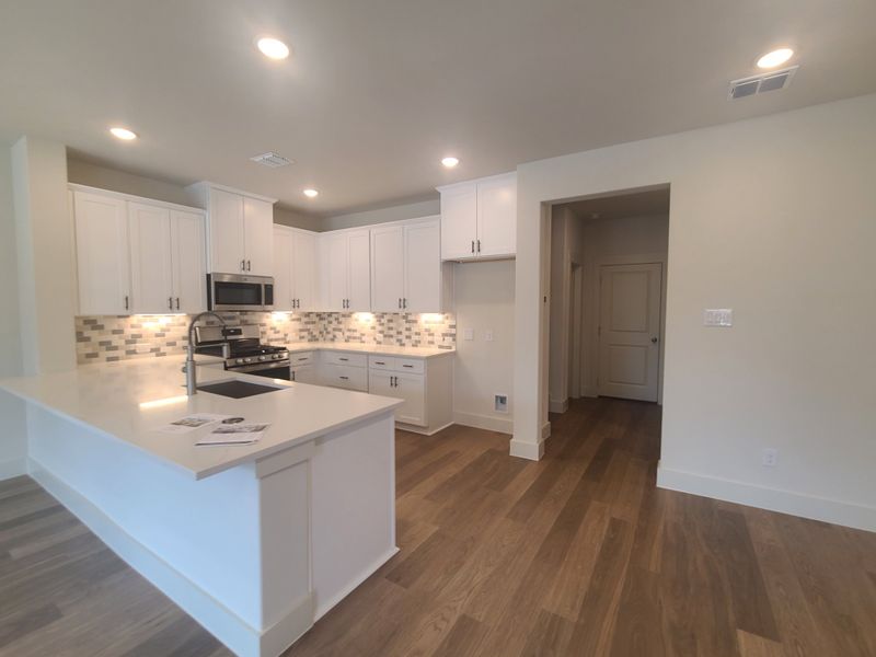 A modern kitchen with white cabinetry, stylish backsplash, and wood flooring.