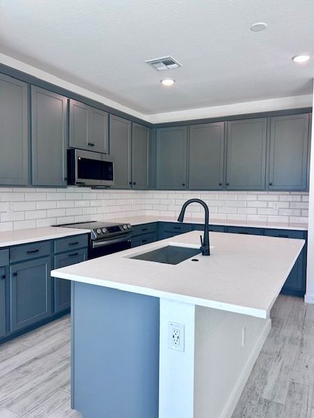 A modern kitchen featuring sleek gray cabinets, a spacious island, and a stylish black faucet. A modern kitchen featuring sleek gray cabinets, a spacious island, and a stylish black faucet.