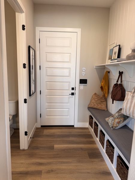A welcoming entryway with wood flooring and built-in bench storage, accented with pillows and hooks for hanging essentials.
