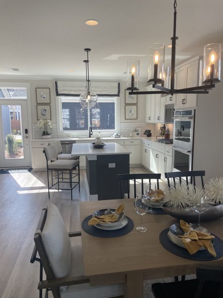 A bright, open-concept kitchen and dining area with white cabinetry, a dark island, modern pendant lighting, and a beautifully set wooden dining table.