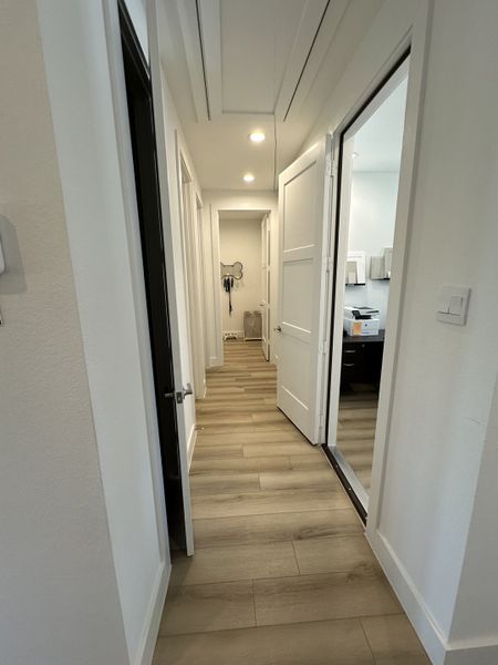 A modern hallway with light wood flooring, white walls, and recessed lighting leading to multiple rooms.