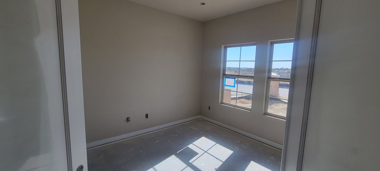 A sunlit room with beige walls, large windows, and unfinished flooring, radiating potential for personalization.