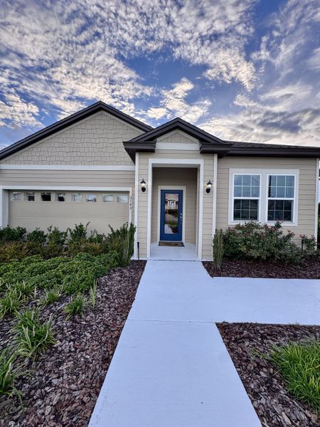 A charming beige home with a blue door and manicured garden in Rolling Hills by LGI Homes (Green Cove Springs, FL).