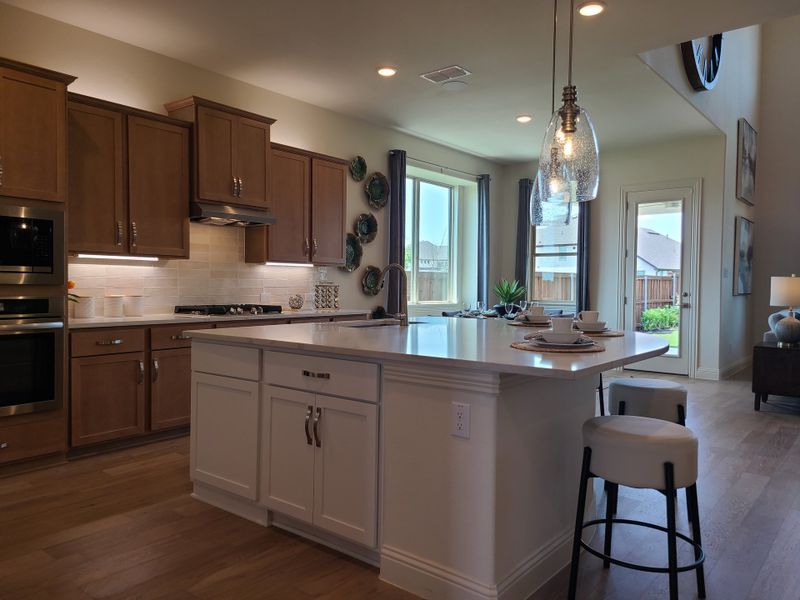A modern kitchen with wood cabinetry, a white island, and chic pendant lights, offering a bright and inviting atmosphere.