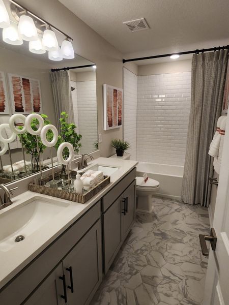 A contemporary bathroom featuring dual sinks, stylish cabinetry, marble-patterned flooring, and elegant lighting.