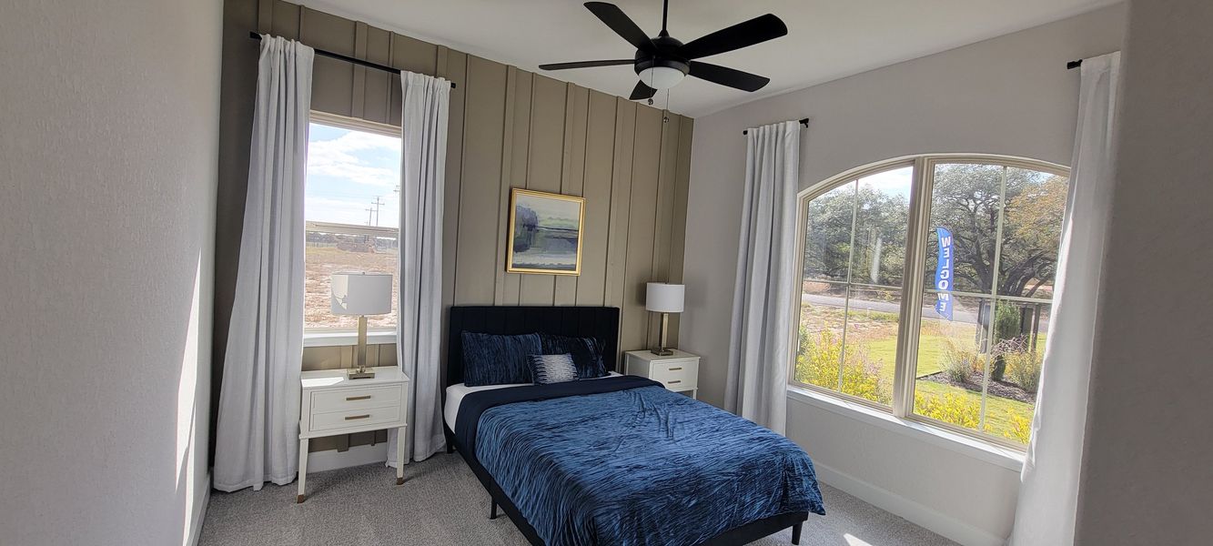 A cozy bedroom with a navy bedspread, white curtains, and ample natural light from large windows creating a serene atmosphere.