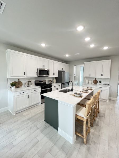 A spacious kitchen featuring sleek white cabinetry, a central island with seating, and modern appliances.