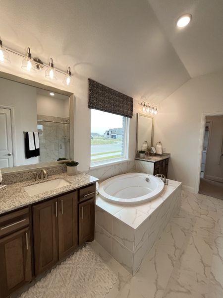 A luxurious bathroom featuring a granite-topped vanity, marble-patterned tiles, and a spacious soaking tub.