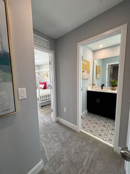 A cozy hallway featuring soft carpet leading to a modern bathroom with patterned tiles and sleek fixtures.