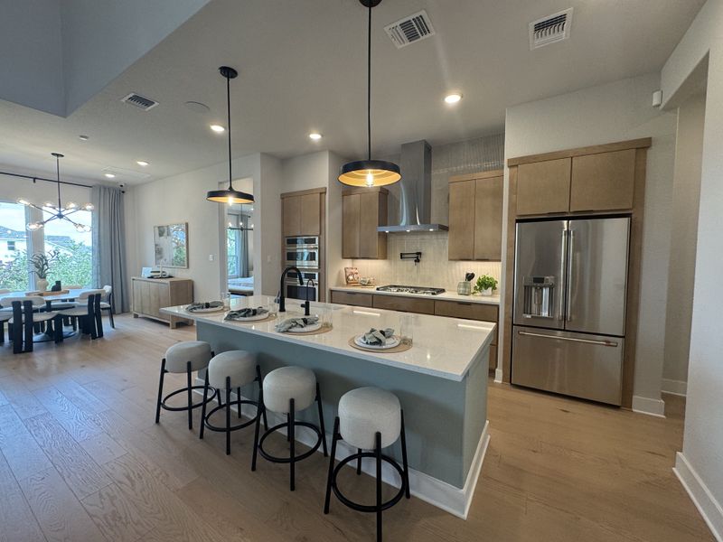 A modern kitchen with sleek wooden cabinets, an island with seating, and pendant lighting, adjacent to a chic dining area.