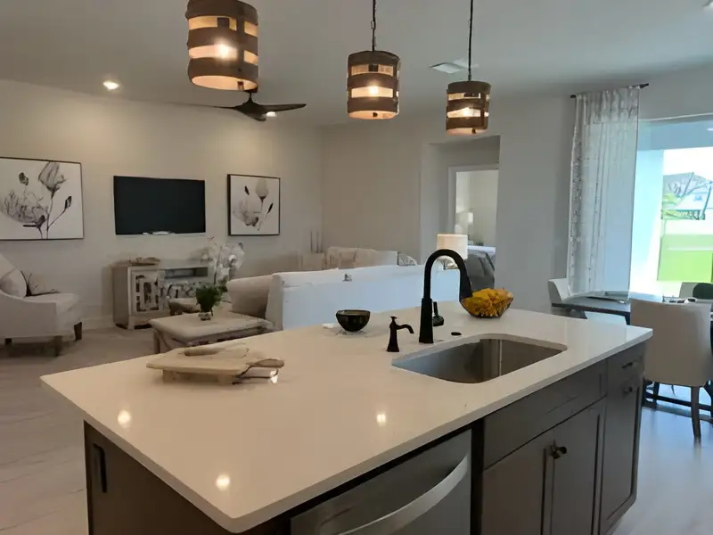 A modern kitchen with a sleek island, pendant lights, and cozy living area featuring elegant decor.
