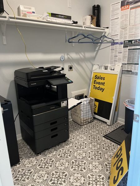 A functional utility room with a patterned tile floor, copier, and shelf storage. Ideal for office or small business use.